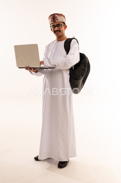 مفهوم الثقافة والتعلم الذاتي، المناهج والمواد التعليمية في عمان , بورترية لشاب عربي خليجي عماني مبتسم يرتدي الدشداشة و الكمه و الحقيبه يقوم بمتابعة الدراسة عبر الحاسب، استخدام الأجهزة التقنية الحديثة لحضور المحاضرات الجامعية، الجسم بالطول الكامل، خلفية بيضاء