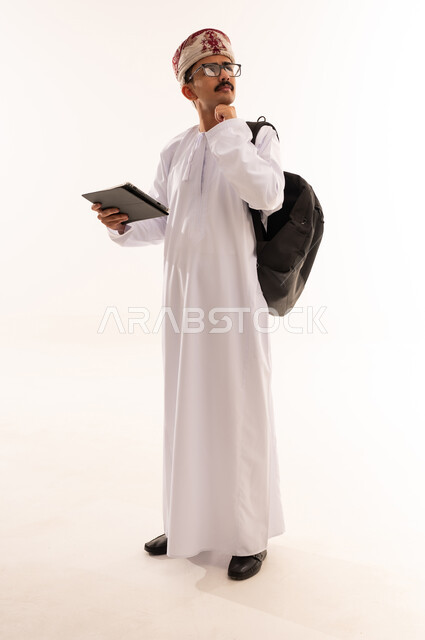 التعلم عن بعد ، إيماءات وجه ويدين تدل على التفكير والحيرة ، بورتريه لطالب جامعي عربي يرتدي الزي الخليجي  العماني يقوم بإجراء مكالمة فيديو من خلال جهاز التابلت ، الإستعداد للمحاضرات الجامعية الالكترونية ، التعليم في  عمان، الجسم بالطول الكامل، خلفية بيضاء