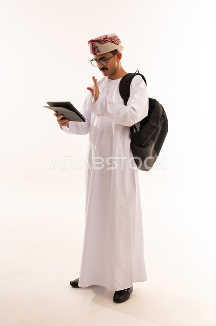 تصفح مواقع التواصل الاجتماعي، متابعة الأفلام والمسلسلات الممتعة، المحادثة مع الأهل والأصدقاء، استعمال التكنولوجيا و التقنيات الحديثة, بورتريه لرجل عربي خليجي عماني يرتدي الدشداشة والكمة وحقيبة جلدية يحمل بيده جهاز التابلت، الطول الكامل للجسم، خلفية بيضاء