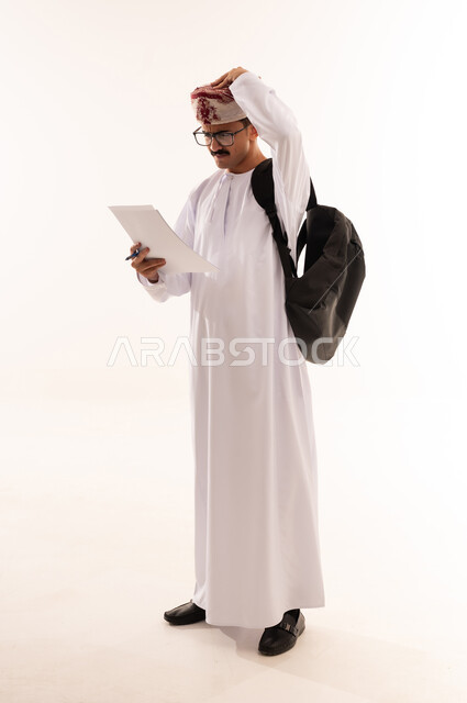 التعليم الجامعي في عمان، إيماءات تدل على التفكير والحيرة ، تدوين الملاحظات وكتابة تقارير وأبحاث علمية ، بورتريه طالب جامعي عربي يرتدي الزي التقليدي و يحمل بيده مجموعة أوراق وعلى ظهره حقيبة ، مراجعة الدروس اليومية ،الجسم بالطول الكامل، خلفية بيضاء