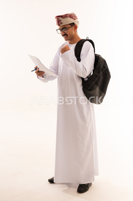 دراسة المحاضرات والمقررات, الاستعداد للعام الجامعي الجديد, بورتريه لطالب عربي خليجي عماني يرتدي الدشداشة والكمة و النظارة الطبية يحمل حقيبة على ظهره يقوم برفع قبضة اليد بايماءات السرور والتفوق, الجسم بالطول الكامل، خلفية بيضاء