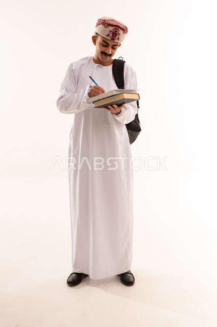 الاستعداد للعام الجامعي الجديد, الجامعات والكليات الأكاديمية في سلطنة عمان, بورتريه لطالب عربي خليجي عماني يرتدي الدشداشة والكمة يحمل حقيبة على ظهره يمسك بيده ورقة وقلم يقوم بمتابعة الدروس اليومية, الجسم بالطول الكامل, خلفية بيضاء