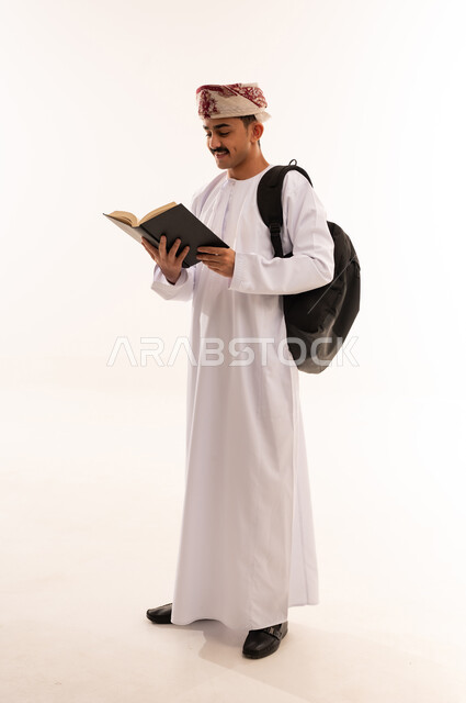 مراجعة الدروس للمذاكرة والاختبارات المدرسية، تطوير المناهج التعليمية في سلطنة عمان، تعابير الاجتهاد والتفوق, بورتريه لطالب جامعي عربي خليجي عماني يرتدي الكمه والدشداشةيقوم بقراءة الكتاب المدرسي بتركيز واندماج, الجسم بالطول الكامل، خلفية بيضاء