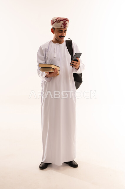 الاستفادة من الأجهزة والتكنولوجيا الحديثة في الاطمئنان على الأقارب، التواصل مع الأهل والأصدقاء وسماع أخبارهم، بورتريه لرجل عربي خليجي عماني يرتدي الدشداشة والكمه و الحقيبة ويمسك الهاتف المحمول بإيماءات السعادة، الجسم بالطول الكامل، خلفية بيضاء