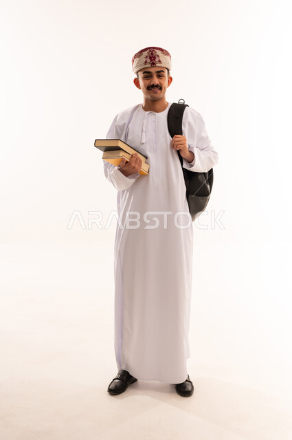 مفهوم الدراسة و التعليم, التعليم العالي في الجامعات والكليات الأكاديمية في سلطنة عمان, النظر بإيماءات السعادة والسرور, بورتريه لطالب عربي خليجي عماني يرتدي الدشداشة والكمة يحمل حقيبة على ظهره, الجسم بالطول الكامل، خلفية بيضاء
