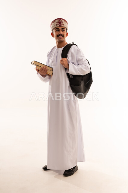 الاستعداد للعام الجامعي الجديد, التعليم العالي في الجامعات والكليات الأكاديمية في سلطنة عمان, النظر بإيماءات السعادة والسرور, بورتريه لطالب عربي خليجي عماني يرتدي الدشداشة والكمة يحمل حقيبة على ظهره, الجسم بالطول الكامل، خلفية بيضاء
