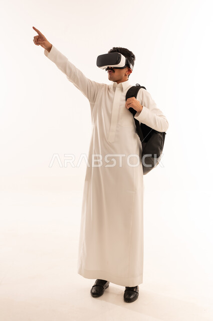 مشاهدة أفلام الواقع الافتراضي، رفع اليد بإيماءات الاندماج ومحاكاة العالم الخيالي، استخدام التقنيات والتكنولوجيا المتطورة، بورتريه لشاب عربي خليجي سعودي يرتدي الزي التقليدي يضع نظارة في آر، قضاء أوقات الفراغ بشكل ممتع، الجسم بالطول الكامل، خلفية بيضاء