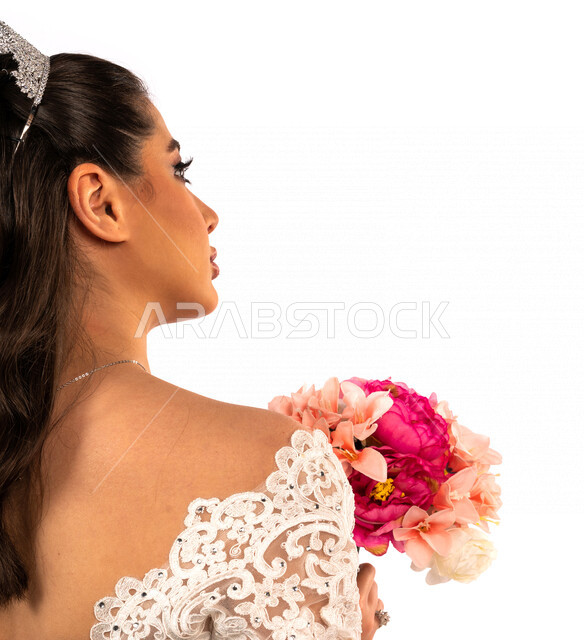 بورتريه بزاويه من الخلف لعروسة عربية خليجية سعودية جميلة تقوم بجلسة تصوير بإيماءات وجه ويدين مختلفة ، أجمل اطلالة لعروسة سعودية عربية خليجية في يوم زفافها ، ترتدي بدلة الزفاف البيضاء ، تحمل بيدها باقة ورد جميلة ، ليلة العمر ، مناسبات وأفراح