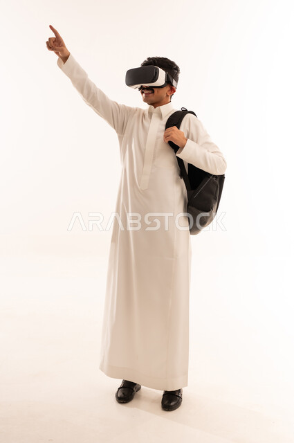 Raising hand with merging gestures and simulating the imaginary world, using advanced techniques and technology, portrait of a young Saudi Arabian Gulf man wearing traditional clothing and VR glasses, watching virtual reality movies, having fun, full body, white background