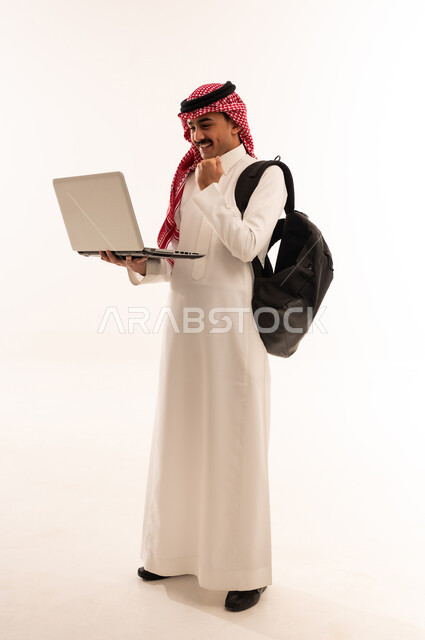 متابعة الدرجات من خلال الحاسب المحمول، بورتريه لطالب جامعى عربي خليجي سعودي يحمل حقيبة الظهر، البحث والمطالعة وتصفح التطبيقات الالكترونية، الاستعداد للعام الدراسي الجامعي الجديد، ايماءات الوجه واليد تدل على النجاح والامتياز، الجسم بالطول الكامل، خلفية بيضاء