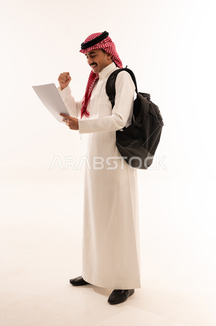 متابعة الدرجات الجامعية، بورتريه لطالب جامعى عربي خليجي سعودي يحمل حقيبة الظهر يمسك بورق جامعي ، البحث والمطالعة، الاستعداد للعام الدراسي الجامعي الجديد، ايماءات الوجه واليد تدل على النجاح والامتياز، الجسم بالطول الكامل، خلفية بيضاء