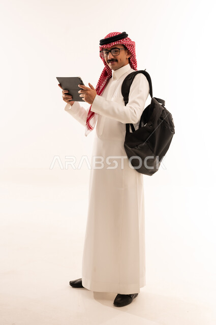 Using modern technology devices, preparing for online lectures, portrait of a smiling Saudi Arabian Gulf student wearing traditional dress making a video call through a tablet, distance learning, reviewing daily lessons, full body, white background
