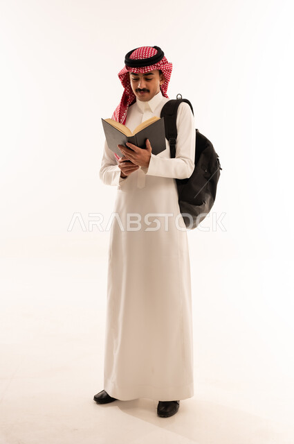 الاجتهاد وتحضير الدروس, تطوير المناهج التعليمية في السعودية, بورتريه لشاب عربي سعودي خليجي مبتسم يرتدي الثوب التقليدي يحمل الحقيبة و يقوم بقراءة الكتب, بداية العام الدراسي الجديد, صورة الجسم بالكامل،الجسم بالطول الكامل، خلفية بيضاء