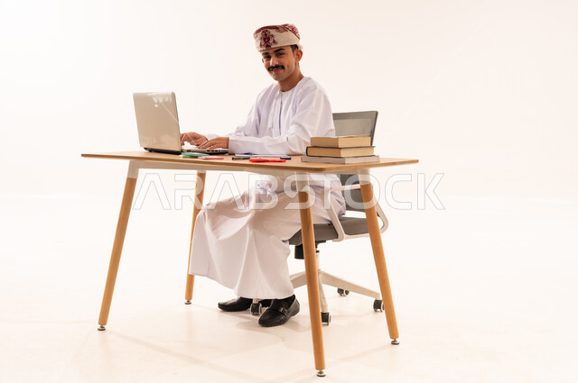 المناهج والمواد التعليمية، دمج التقنيات الحديثة بالتعليم الأكاديمي, مفهوم الاجتهاد والتفوق, بورتريه لطالب جامعي عربي خليجي عماني مبتسم يرتدي الكمة و الدشداشة ويقوم باستعمال جهاز الحاسوب المحمول,إيماءات الإجتهاد والاهتمام بالعلم والتعلم ، خلفية بيضاء
