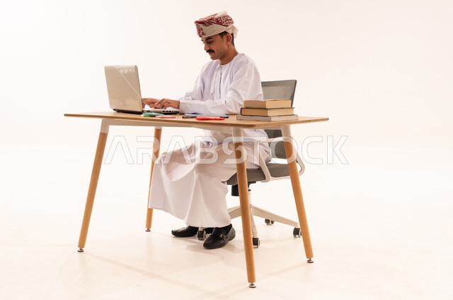 دمج التقنيات الحديثة بالتعليم الأكاديمي, مفهوم الاجتهاد والتفوق, المناهج والمواد التعليمية, بورتريه لطالب جامعي عربي خليجي عماني مبتسم يرتدي الكمة و الدشداشة ويقوم باستعمال جهاز الحاسوب المحمول,إيماءات الإجتهاد والاهتمام بالعلم والتعلم ، خلفية بيضاء
