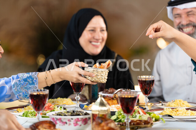 الاحتفال بقدوم شهر رمضان المبارك، مائدة طعام مليئة بأصناف من المأكولات والمقبلات الشهية, ايماءات السعادة بقضاء اوقات ممتعه مع الاهل، صورة مقربة ليد امراة عربيه خليجيه اماراتية تقوم بتقديم طبق من الحلويات الشرقية، اسلاميات وعبادات رمضانية