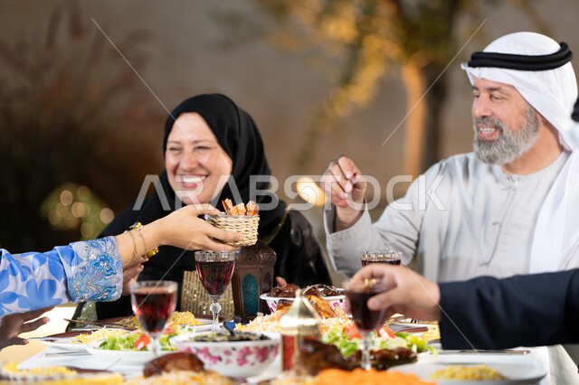 اسلاميات وعبادات رمضانية، نقاشات و حوارات عائليه على مائدة الطعام, سفرة مليئة بالمأكولات والمشروبات، قضاء أوقات عائليه ممتعه، صورة مقربة ليد امراة عربيه خليجيه اماراتية تقوم بتقديم طبق من الحلويات الشرقية، إيماءات السعادة والسرور
