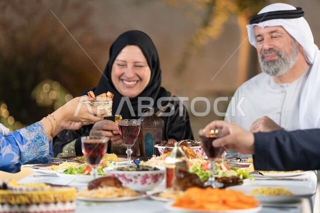 نقاشات و حوارات عائليه على مائدة الطعام, سفرة مليئة بالمأكولات والمشروبات، قضاء أوقات عائليه ممتعه، صورة مقربة ليد امراة عربيه خليجيه اماراتية تقوم بتقديم طبق من الحلويات الشرقية، إيماءات السعادة والسرور، اسلاميات وعبادات رمضانية