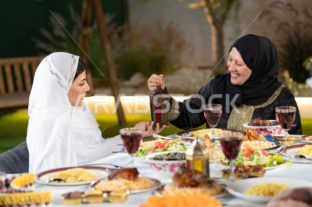 تبادل الأحاديث بين أفراد الأسرة، أجواء عائلية دينية رمضانية سعيدة، سفرة مليئة بأصناف من المأكولات الشرقية الشهية، أداء فريضة الصيام في شهر رمضان المبارك، امراة عربية خليجيه اماراتية تقوم بتقديم الفانوس لابنتها بايماءات السعاده و السرور