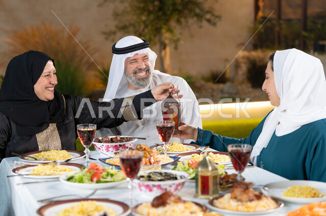 نقاشات وحوارات عائلية، مائدة طعام مليئة بالوجبات الرمضانية المتنوعة، لحظات روحانية رمضانية، الإستمتاع باجواء رمضان مع الأهل، أجواء أسرية مليئة بالحب، ام عربية خليجيه اماراتية تقوم بتقديم فانوس رمضان لابنتها بايماءات السعاده و السرور