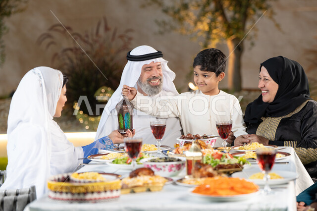 الإستمتاع  باجواء رمضان مع الأهل، مائدة طعام مليئة بالوجبات الرمضانية المتنوعة، نقاشات وحوارات عائلية، أجواء أسرية مليئة بالحب، اجتماع الاسرة حول مائدة الطعام، ولد عربى خليجي اماراتي يقوم بتقديم فانوس رمضان لوالدته بايماءات السعاده و السرور