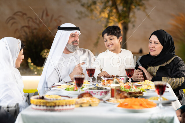 العزائم والولائم في الأعياد والمناسبات الإسلامية، مائدة طعام مليئة بالوجبات الرمضانية المتنوعة، نقاشات وحوارات عائلية، أجواء أسرية مليئة بالحب، اجتماع الاسرة حول مائدة الطعام، عائلة عربية خليجيه إماراتيه تستعد لتناول الفطار