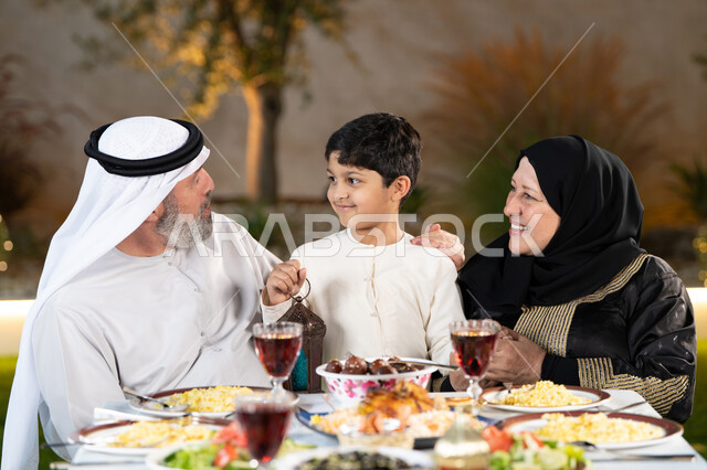 جلسة عائلية رمضانية روحانية، اجتماع الاسرة حول مائدة الطعام، عائلة عربية خليجيه إماراتيه تستعد لتناول الفطار، سفرة مليئة بأصناف من المأكولات والمقبلات الشهية، تبادل الأحاديث والنقاشات بإيماءات السعادة والسرور
