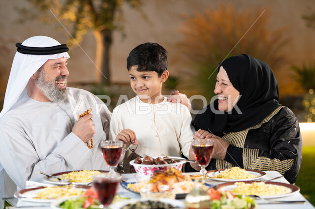 تبادل الأحاديث والنقاشات بإيماءات السعادة والسرور، اسلاميات وعبادات رمضانية، اجتماع الاسرة حول مائدة الطعام، عائلة عربية خليجيه  إماراتيه تستعد لتناول الفطار، سفرة مليئة بأصناف من المأكولات والمقبلات الشهية