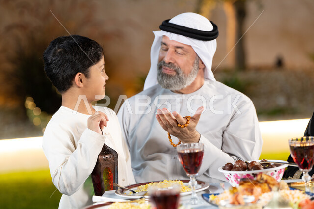 أجواء عائلية رمضانيه، فرحة الابناء بقدوم الشهر المبارك, صبى عربي خليجي اماراتي مبتسم يحمل فانوس رمضان و يشارك جده الفرحة, أداء فريضة الصيام ، سفرة إفطار مليئة بأصناف من المأكولات والمقبلات الشهي، ايماءات السعادة و السرور