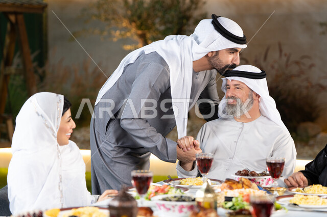 أداء فريضة الصيام في شهر رمضان المبارك، سفرة إفطار مليئة بأصناف من المأكولات والمقبلات الشهية, عائلة عربية خليجية إماراتية مستمتعة بتناول الفطور, مشاركة الطعام وإكرام الوالدين، شاب اماراتي خليجي يقوم بتقبيل رأس والده، التربية الصالحة للأبناء