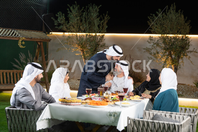 الاحتفال بالاعياد و المناسبات الاسلامية، سفرة إفطار مليئة بأصناف من المأكولات والمقبلات الشهية, عائلة عربية خليجية إماراتية مستمتعة بتناول الفطور في شهر رمضان, مشاركة الطعام وإكرام الوالدين، شاب اماراتي خليجي يقوم بتقبيل رأس والده، التربية الصالحة للأبناء