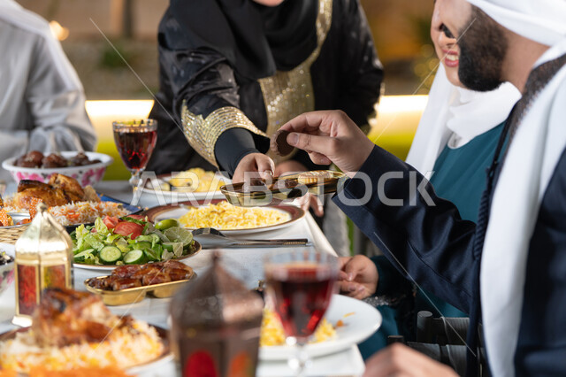 حسن الضيافة والاستقبال في شهر رمضان المبارك،  صورة مقربة لعائله عربيه خليجيه اماراتية تجتمع حول مائده الطعام ، امراة خليجيه تقوم بتقديم طبق من الحلوي الشهيه ، أداء فريضة الصيام
