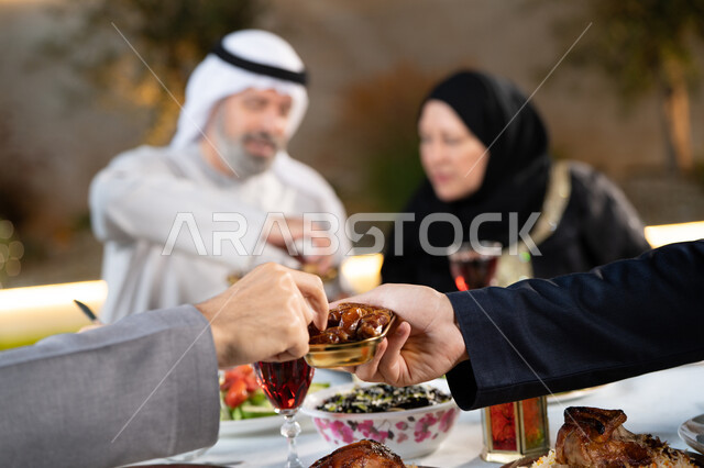 Breaking the fast at sunset, a famous Ramadan dessert, a close-up of an Arab man's hand holding a plate full of delicious Luqaimat sweets, hospitality and reception in the holy month of Ramadan, an Arab Gulf Emirati family gathering around food