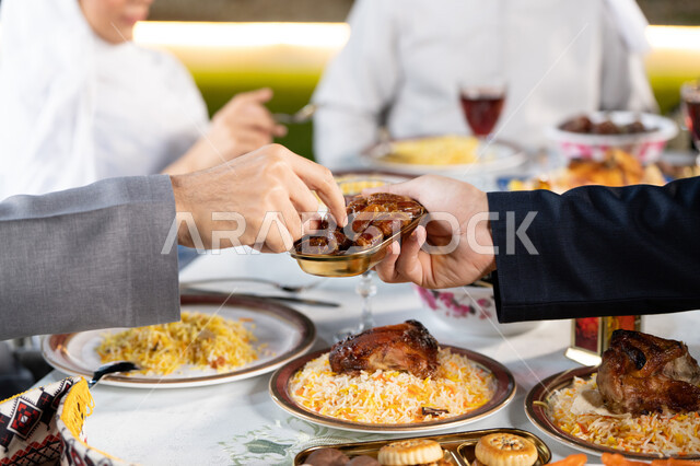 حلى رمضاني شهير، صورة مقربة ليد رجل عربي يحمل بيده صحن مليء بحلوى اللقيمات الشهية، حسن الضيافة والاستقبال في شهر رمضان المبارك، الأجواء الرمضانية الروحانية، عائله عربية خليجيه اماراتية تجتمع حول الطعام