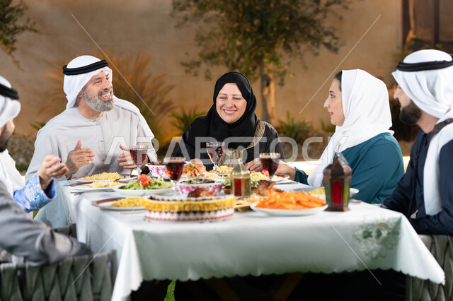 قضاء أوقات ممتعة مع الاسرة ، سفرة مليئة باصناف من المأكولات الشرقية الشهية، اجتماع العائلة حول مائدة الطعام، أداء فريضة الصيام، أجواء دينية رمضانية، أسرة عربية خليجية اماراتية تقوم بتبادل الأحاديث والنقاشات بإيماءات السعادة والسرور
