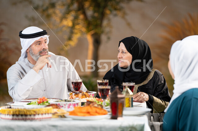 أداء فريضة الصيام، أجواء دينية رمضانية، أسرة عربية خليجية اماراتية تقوم بتبادل الأحاديث والنقاشات بإيماءات السعادة والسرور، اجتماع العائلة حول مائدة الطعام، سفرة مليئة باصناف من المأكولات الشرقية الشهية