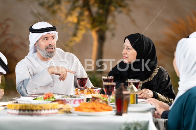 أجواء دينية رمضانية، أسرة عربية خليجية اماراتية تقوم بتبادل الأحاديث والنقاشات بإيماءات السعادة والسرور، اجتماع العائلة حول مائدة الطعام، سفرة مليئة باصناف من المأكولات الشرقية الشهية، أداء فريضة الصيام