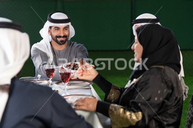 تجمعات العائلة على افطار رمضان، الكرم والمشاركة خلال وقت الإفطار، رجل خليجي إماراتي يقدم طبق التمر لأحد أفراد العائلة، ايماءات السعادة و السرور بقدوم شهر رمضان المبارك, حسن الضيافه والإستقبال