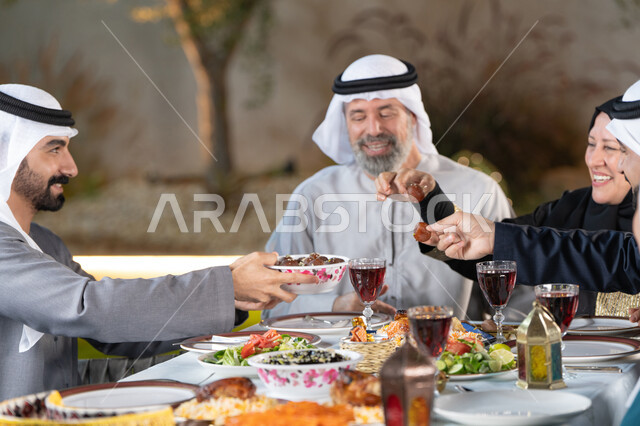 مائدة إفطار مليئة بالأصناف والمأكولات الشهية، حسن الضيافه والإستقبال, إفطار صائم، قضاء أوقات ممتعة مع العائلة في الهواء الطلق،عائلة عربية خليجية إماراتية تقوم بتناول الافطار بايماءات السعادة و السرور، رجل خليجي يقوم بتقديم طبق التمر للضيوف