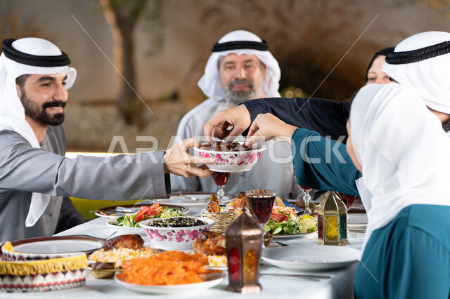 Spending fun times with the family outdoors, an Iftar table full of delicious dishes and foods, an Arab Gulf Emirati family eating dates with gestures of happiness and pleasure, the holy month and the spiritual Ramadan atmosphere