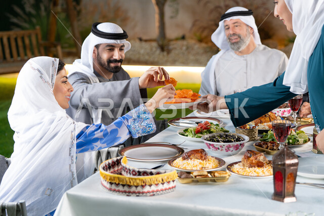 الكرم وتقديم أشهى المأكولات و الحلويات ، طاولة رمضانية مزينة بالفوانيس المضيئة, مائدة مليئة بأصناف الطعام المختلفة, الاجتماع حول سفرة الافطار، عائله عربيه خليجيه اماراتية يقومون بتناول الافطار، ايماءات السعادة و السرور بقدوم شهر رمضان المبارك