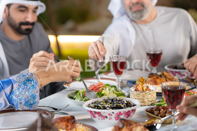 أداء فريضة الصيام، أجواء دينية رمضانية، اجتماع الأسرة حول مائدة الطعام، سفرة مليئة باصناف من المأكولات و المشروبات الشهية، صورة مقربة ليد امراة عربيه خليجيه اماراتية تقوم بتناول السلطه الشهيه
