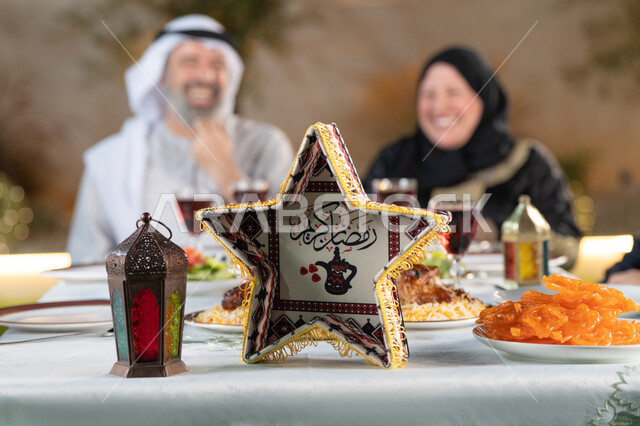 نقاش وحوار عائلي، ديكور وأجواء رمضانية، مائده طعام مليئه بأصناف المأكولات و المقبلات الشهية، زوجان عربيان خليجان اماراتيان حول سفرة الإفطار في شهر رمضان المبارك، ايماءات السعادة والسرور