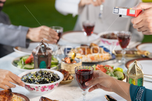 كسر الصيام عند سماع أذان المغرب، قضاء أوقات ممتعه مع العائله في الخارج، أسرة عربيه خليجيه اماراتية تقوم بتناول الطعام العائلي في أحد المطاعم، مائده إفطار مليئه بالأصناف والمأكولات الشهية، ديكورات وأجواء رمضانيه.