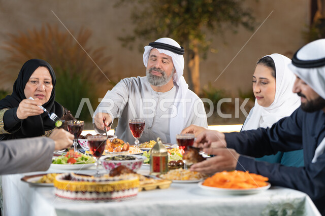 مائده طعام مليئه بأصناف المأكولات و المقبلات الشهية، ديكور وأجواء رمضانية، نقاش وحوار عائلي، تجمع أسرة عربية خليجية اماراتية حول سفرة الإفطار في شهر رمضان المبارك، ايماءات السعادة والسرور
