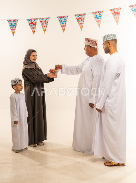 إظهار مشاعر الفرح والسعادة بقدوم العيد، مفهوم الحنان والمحبة والمودة،  بورتريه لعائلة عربية خليجية عمانية  ترتدي الملابس العمانية التقليدية وتقوم بتبادل المعايدات, تقديم الضيافة العربية والحلويات الشعبية، الزيارات العائلية والاحتفال بالأعياد الإسلامية، خلفية بيضاء .