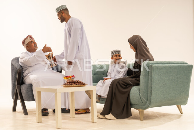 زينة وديكورات رمضانية ، التجمعات العائلية السعيدة في شهر رمضان المبارك، فوانيس وزينة الأعياد والمناسبات الاسلامية في سلطنة عمان، بورتريه لعائلة عربية خليجية عمانية ترتدي الملابس العمانية التقليدية تجلس فى غرفة المعيشة ،تقوم بتبادل المعايدات,  خلفية بيضاء .