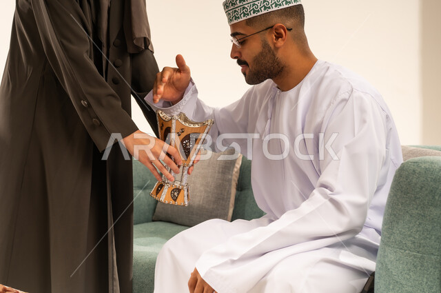 زينة وديكورات رمضانية ، الاستعداد لاستقبال شهر رمضان المبارك بإيماءات السرور، فوانيس وزينة الأعياد والمناسبات الاسلامية في سلطنة عمان، صورة مقربة ليد امرأة عربية خليجية عمانية تقوم باضاءة فانوس رمضان لزوجها ,  خلفية بيضاء .