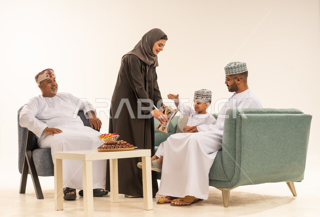 فوانيس وزينة الأعياد والمناسبات الاسلامية في سلطنة عمان، بورتريه لعائلة عربية خليجية عمانية ترتدي الملابس العمانية التقليدية تجلس فى غرفة المعيشة ،تقوم بتبادل المعايدات, الاستعداد لاستقبال شهر رمضان المبارك بإيماءات السرور، خلفية بيضاء
