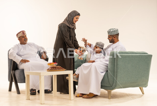 Eid morning celebrations, offering Arab hospitality and traditional sweets, family visits and celebrating Islamic holidays, a portrait of an Omani Gulf Arab family sitting in the living room exchanging greetings, showing feelings of joy and happiness at the arrival of Eid, the concept of tenderness, love and affection, white background.